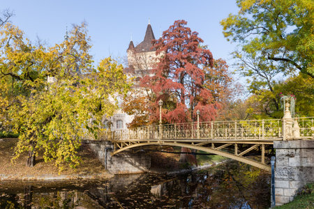Decorative arched metal riveted footbridge over the canal painted in yellow in the autumn City park against the southern facade of the Vajdahunyad Castle at sunny day, Budapestの写真素材