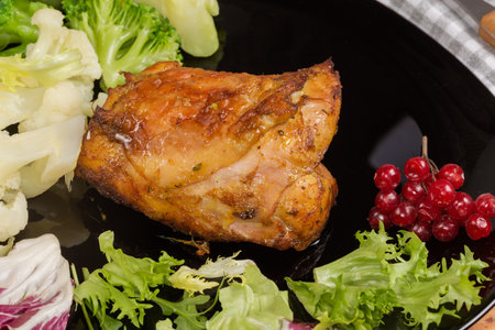 Crispy baked chicken thigh among the boiled broccoli and cauliflower pieces and fresh leaf vegetables on the black dish, close-upの写真素材