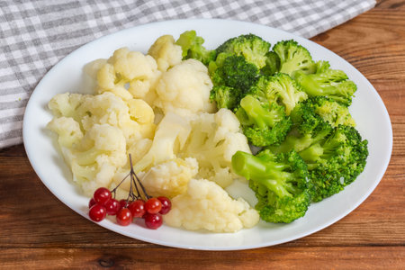 Freshly boiled small pieces of broccoli and cauliflower on the white dish decorated with viburnum berries on a rustic table, close-upの写真素材