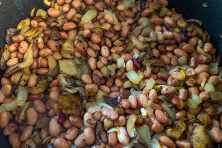 Cultivated oyster mushrooms with chopped onion and boiled beans during frying with cooking oil in...
