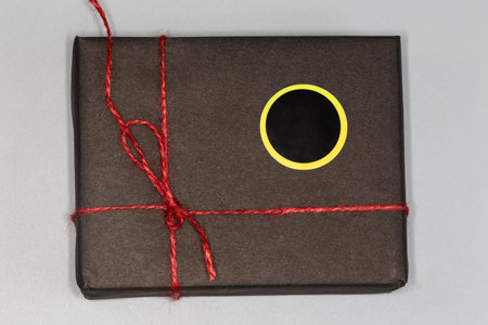 Small rectangular box wrapped in black wrapping paper with blank round yellow-black sticker and...