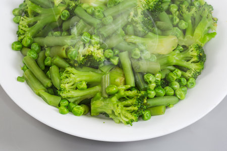 Freshly boiled mixture of the different green vegetables on a white dish, top view of fragment close-up on a gray backgroundの写真素材