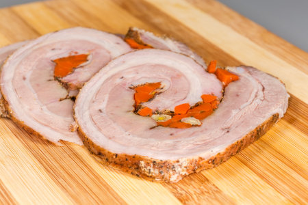 Slices of the baked meat roll made with pork belly with vegetables on a wooden cutting board, side view close-up in selective focusの写真素材