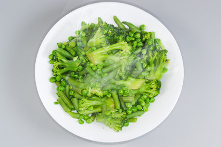 Freshly boiled mixture of the different green vegetables on a white dish, top view on a gray backgroundの写真素材