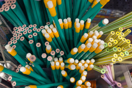 Heap of different graphite pencils painted in various colors with and without eraser attachments on ends for sale, top view from the end sides close-up in selective focusの写真素材