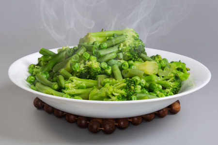 Freshly boiled mixture of the different green vegetables on a white dish on a stand for hotの写真素材