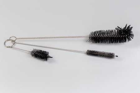 Three different kitchen, or laboratory cleaning brushes for hard-to-reach places made with twisted metal wire and nylon bristles on the edge on a gray surfaceの写真素材