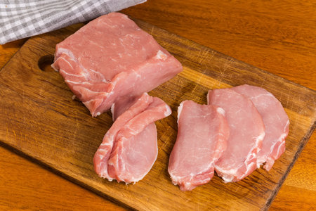Piece and several slices of raw boneless pork loin on a wooden cutting board on a table, top viewの写真素材