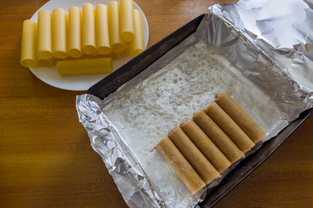 Preparation of the stuffed large cylindrical cannelloni pasta with meat filling for baking on a baking tray covered with foil, top viewの写真素材