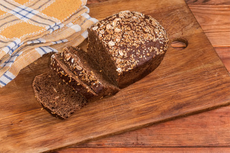 Partially sliced brown grain bread, made with rye and wheat flour, decorated with seeds of sesame...