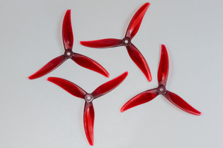 Kit of the red plastic trilobate propellers for a FPV drone with one-piece bases with blades, top view on a gray surfaceの写真素材
