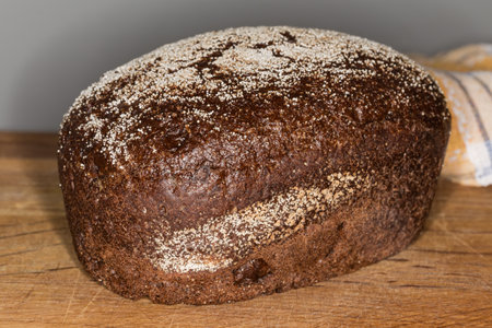Whole loaf of the rye with wheat brown bread sprinkled with semolina on a wooden cutting board, front view close-up on a dark backgroundの写真素材