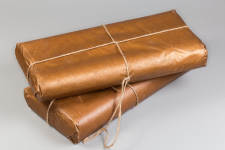 Two stacked rectangular flat item with rounded edges wrapped in light brown wrapping paper and criss-cross tied with ropes on a gray backgroundの写真素材