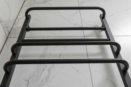 Part of empty black electric heated towel rail installed on a gray tiled wall in the bathroom,...