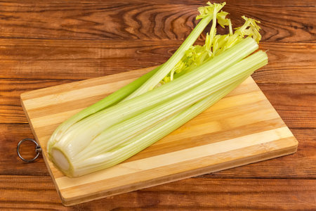 Fresh stems of celery with cropped leaves on a wooden cutting board on an old rustic tableの写真素材
