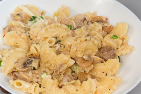 Freshly cooked short curved ruffled pasta, so called Creste di gallo, or rooster's comb with mushrooms and cheese in white souse on a dish, fragment close-upの写真素材