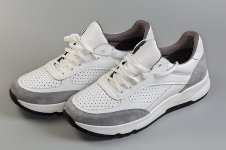 Pair of the white leather sneakers of classic style with gray inserts on the toecaps and backs and lacing on a gray backgroundの写真素材