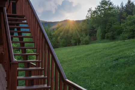 External straight wooden stairs of the building with handrail against mountain forested slope at sunsetの写真素材