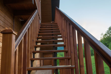 External straight wooden stairs of the building with handrail in sunny evening, bottom-up view backlitの写真素材