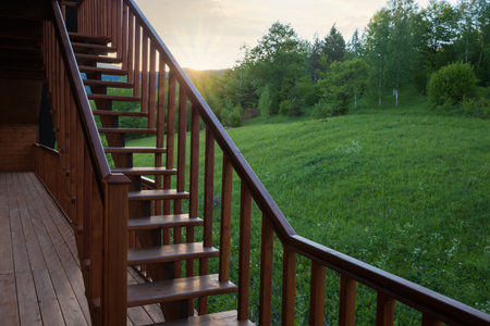 External straight wooden stairs of the building with handrail against mountain forested slope at sunsetの写真素材