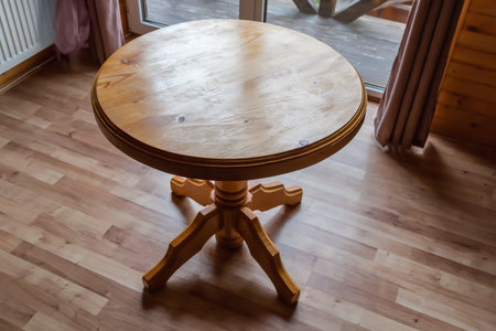 Wooden table on one leg with round table top stand in room with wooden flooring opposite the panoramic window backlitの写真素材