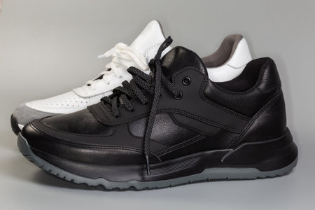 One black and one white leather sneaker of classic style with lacing on a gray background, side view in selective focusの写真素材