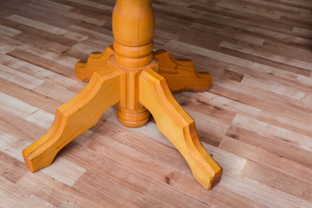 Figured leg of the wooden single leg table standing in room with wooden flooring, close-upの写真素材
