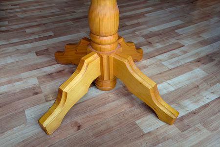 Figured leg of the wooden single leg table standing in room with wooden flooring, close-upの写真素材