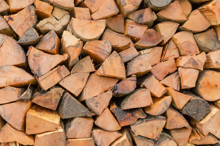 Woodpile of firewood in the form of logs of deciduous trees split along the grain and stacked in a row outdoors, view close-up in overcast rainy dayの写真素材