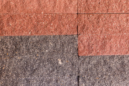 Part of the building wall faced with rectangular red and gray stone tiles with rough front surfaceの写真素材