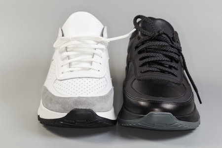 One black and one white leather sneaker of classic style with lacing on a gray background, view from the toecaps side in selective focusの写真素材
