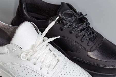 Lacings of one black and one white leather sneaker of classic style on a gray background, fragmentの写真素材