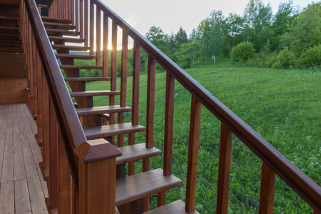 External straight wooden stairs of the building with handrail against mountain forested slope at sunsetの写真素材