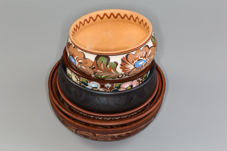 Stack of the different empty clay bowls fired using different technologies and decorated with various traditional folk floral ornaments on a gray backgroundの写真素材