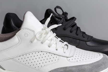 Lacings of one black and one white leather sneaker of classic style on a gray background, side view of fragment in selective focusの写真素材
