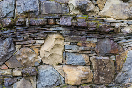 Surface of the wet rough retaining wall built with natural stones different forms, colors and sizes and partially overgrown with moss in rainy overcast dayの写真素材