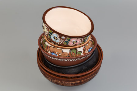 Stack of the different empty clay bowls fired using different technologies and decorated with various traditional folk floral ornaments on a gray backgroundの写真素材