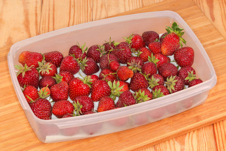 Freshly harvested unwashed organically grown garden strawberries in the rectangular flat plastic container on a wooden cutting board on a rustic tableの写真素材