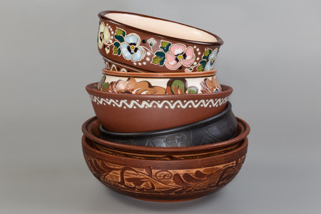 Stack of the different empty clay bowls fired using different technologies and decorated with various traditional folk floral ornaments on a gray background, front viewの写真素材