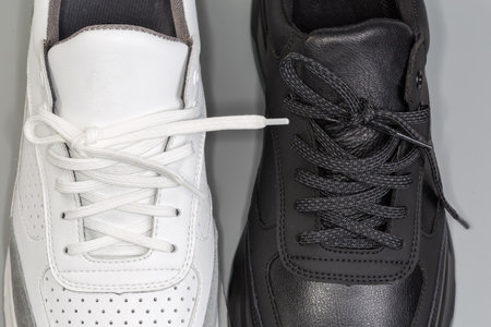 Lacings of one black and one white leather sneaker of classic style on a gray background, top view of fragmentの写真素材