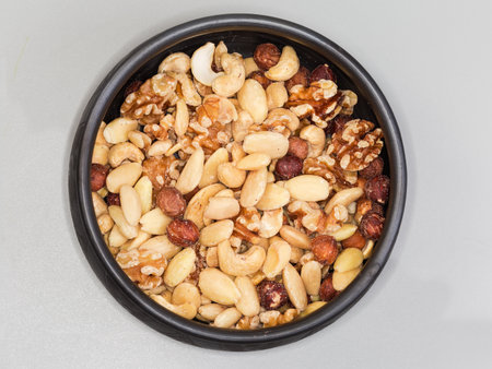 Mixture of the kernels of different nuts peeled from the their shells in a black clay bowl, top view on a gray surfaceの写真素材