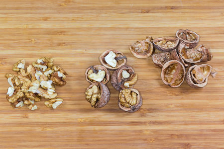 Small heap of the peeled cores of walnuts, the same walnuts split in half and their empty shells separately on a wooden surfaceの写真素材