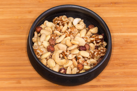 Mixture of the kernels of different nuts peeled from the their shells in a black clay bowl on a wooden surfaceの写真素材