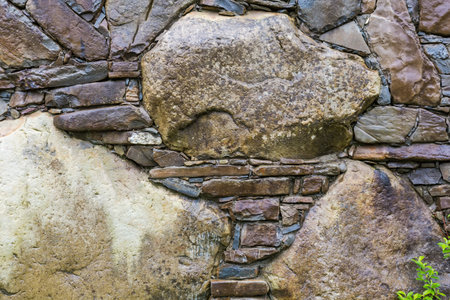 Surface of the wet rough retaining wall built with natural stones different forms, colors and sizes,...