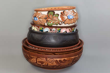 Stack of the different empty clay bowls fired using different technologies and decorated with various traditional folk floral ornaments on a gray background, front viewの写真素材