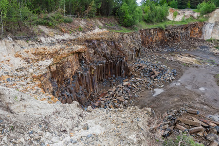 Basaltic columns on the wall of the operating basalt quarry located among the forest, top view in...