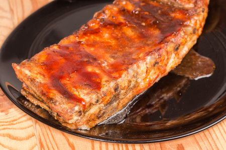 Whole piece of the pork ribs baked in special sauce lies on a big black plate on a table, fragment close-up in selective focusの写真素材