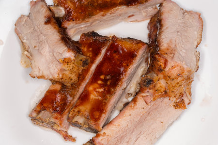 Sliced pork ribs, baked in special sauce lie on a white plate, top view of fragment close-upの写真素材