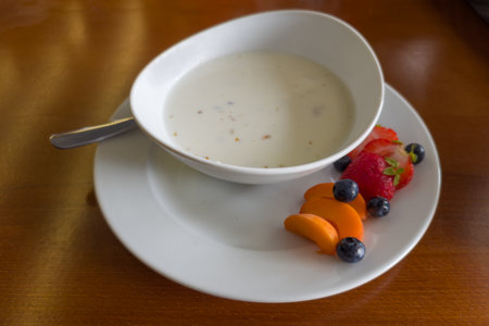 Breakfast of milk oat porridge in bowl and served with several fresh fruits and berries separately on a wooden table, view close-up in selective focusの写真素材
