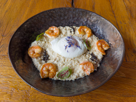Breakfast of poached egg served with oat porridge and grilled prawn tails on the dark dish on an old oak table, top viewの写真素材
